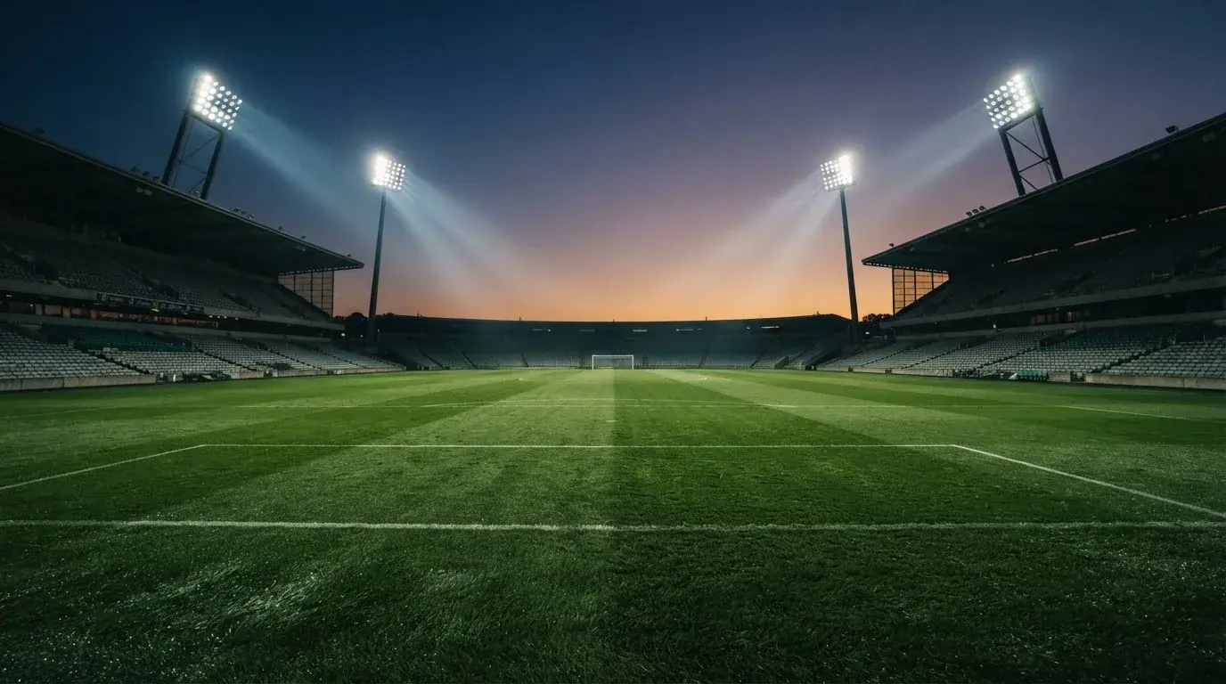 Een leeg voetbalstadion met lichtmasten bij schemering