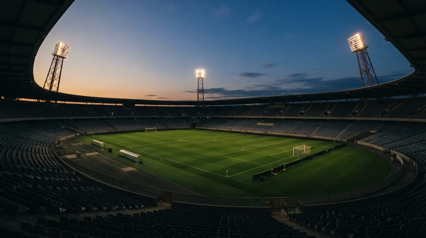 Een leeg voetbalstadion met lichtmasten bij schemering