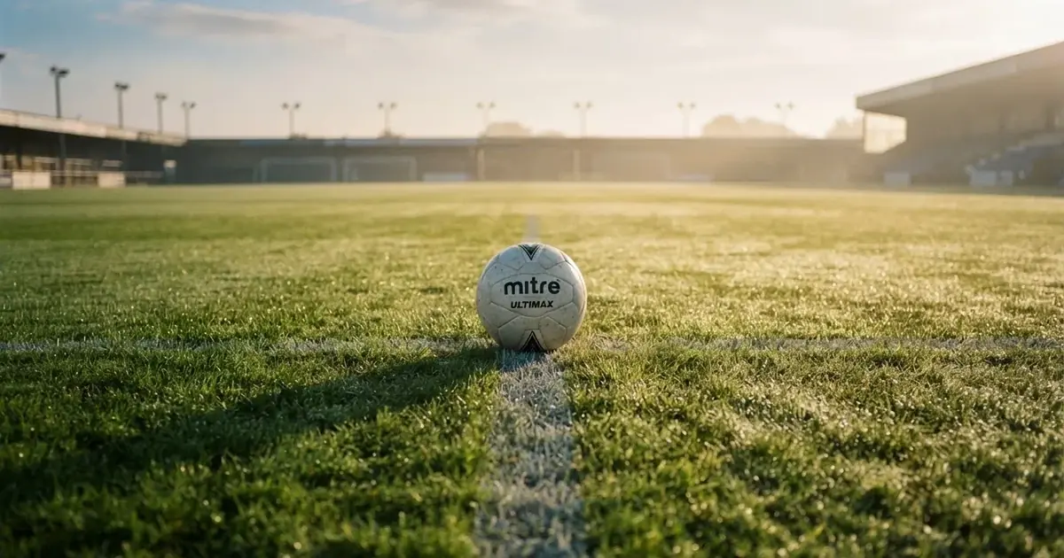 Een voetbal op de middenstip van een grasveld in het ochtendlicht
